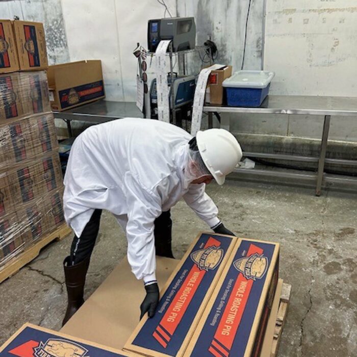 A worker wearing a white coat, white helmet, and face mask is stacking boxes labeled 